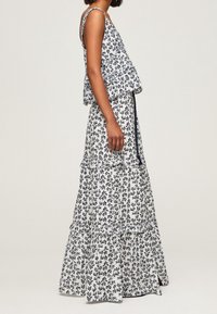 Blumendruckkleid in Weiß und Marineblau mit einem gestuften, gerafften Saum. Verfügt über verstellbare Träger und eine lockere, fließende Silhouette.