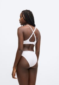 Hvid bomulds bralette med krydsede stropper på ryggen og elastik med mærke under barmen. Matchende trusse med høj talje og logobånd i taljen.