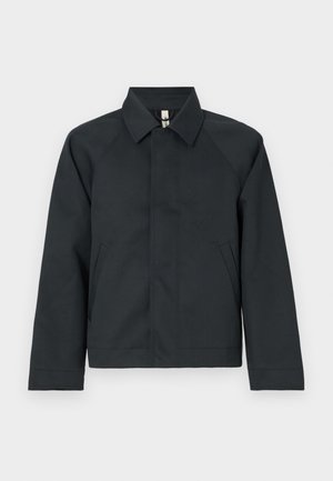 Jachetă închisă la culoare, cu guler, cu mâneci raglan, realizată dintr-un material neted. Dispune de două buzunare laterale și o margine dreaptă, cu detalii minime.