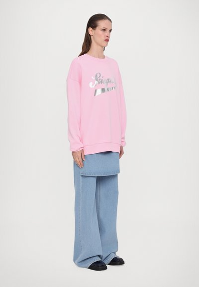 Felpa rosa con branding metallizzato argento, abbinata a pantaloni in denim azzurro a gamba larga. Tessuto morbido e vestibilità comoda. Scarpe nere.