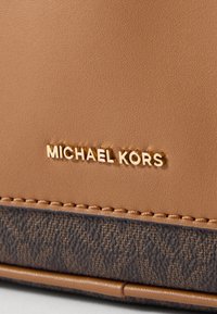 Portafoglio in pelle tan con fondo testurizzato di colore più scuro. Presenta il logo "MICHAEL KORS" impresso in oro. Cuciture visibili lungo i bordi.