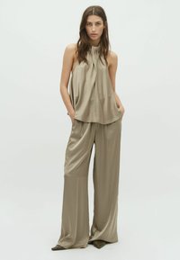 Beige sleeveless top with gathered neckline, paired with loose-fitting, wide-legged pants in matching fabric and color, featuring pockets.