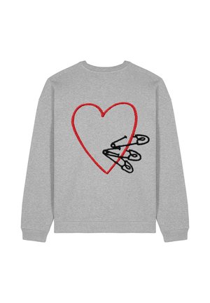 Personne portant un sweat-shirt oversize gris clair, un jean bleu clair taille haute avec revers, et des baskets blanches épaisses, debout les mains dans les poches.
