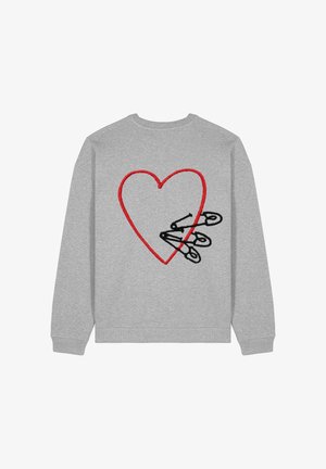 Personne portant un sweat-shirt oversize gris clair, un jean bleu clair taille haute avec revers, et des baskets blanches épaisses, debout les mains dans les poches.