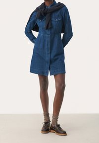 Tummansininen farkkupaita mekko pitkillä hihoilla, rintataskuilla ja muotoiltu vyötärö. Yhdistetty ruskeisiin kenkiin ja ribattuihin ruskeisiin sukkiin.