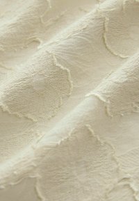 Gros plan sur un tissu beige avec des motifs en relief en forme de cœur et des plis doux.