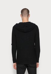 Svart huvtröja med ribbad textur, långa ärmar och lös passform, med dragsko på luvan och rak nederkant.