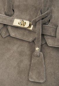 Szara zamszowa torba z klamrą z złotego metalu i teksturowanym paskiem. Projekt obejmuje trójkątną klapę oraz małą zawieszkę.