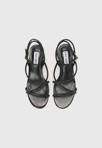 Sandales noires à lanières avec une semelle en cuir lisse et des lanières brillantes et arrondies. Comprend une bride de cheville réglable et une semelle plate.