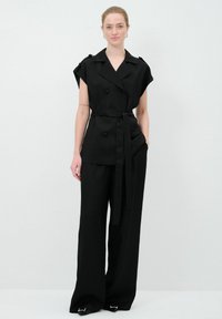 Ensemble sur mesure noir comprenant un haut à double boutonnage à manches courtes avec ceinture à nouer et un pantalon large, tous deux en tissu lisse.