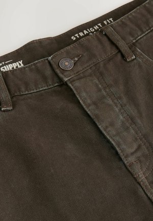 Tiesios kirpimo rudos spalvos kelnės su tekstūruotu audiniu, metaliniu mygtuko uždarymu ir džinsinio stiliaus siuvimo detalėmis juosmens ir užtrauktuko srityse.