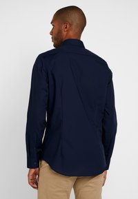 Granatowa koszula z długim rękawem, z kołnierzykiem typu point, dopasowany krój i mankiety zapinane na guziki, wykonana z gładkiego materiału z karczkiem na plecach i bocznymi zaszewkami.