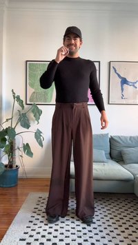 Μαύρο εφαρμοστό μπλούζα με μακριά μανίκια και καφέ ψηλόμεσα, φαρδιά παντελόνια. Εσωτερικός χώρος με μια γλάστρα και καναπέ στο φόντο.