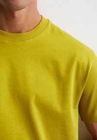 Żółta koszulka z krótkim rękawem wykonana z miękkiej bawełny. Charakteryzuje się prążkowanym okrągłym dekoltem oraz gładką teksturą, podkreślającą prosty, minimalistyczny design.