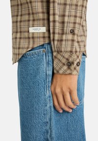 Braun- und cremefarbener kariert Flanellhemd mit geknöpften Manschetten, kombiniert mit hellblauen Jeans aus Denim mit Seitentaschen und einem ausgewaschenen Look.