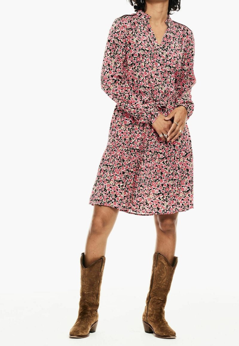 Blommig klänning i rosa och svart tyg, med V-ringning, långa ärmar och åtsittande midja. Kombinerad med ljusbruna cowboystövlar.