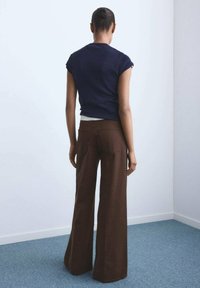 Marineblauw kortmouwtopje en bruine wijde broek. Het topje heeft een getailleerd ontwerp; de broek is high-waisted met een gladde textuur en gedefinieerde naden.
