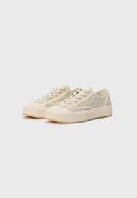 Beige canvas sneakers met gestructureerde zijkanten, gouden veterogen en een stevige crèmekleurige zool; subtiel merklogo aan de zijkant.