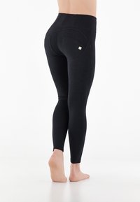 Leggings noires avec une taille haute, texture lisse et deux poches arrière. Présente un détail de logo sur la poche droite.