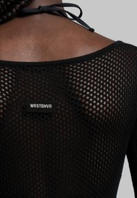 Svart mesh-top med en lös design, rundad halsringning och justerbart snöre i ryggen. Inkluderar en sydd etikett med texten "WRSTBHV".