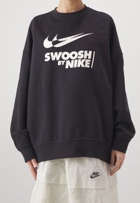 Felpa nera in cotone con collo rotondo, caratterizzata da un grande logo bianco "Swoosh by Nike", vestibilità comoda e polsini a costine.