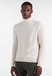 Kerman neule turtleneck, jossa on pehmeä rakenne, istuvat pitkät hihat ja ribattu helma. Edessä on hienovarainen logo rinnassa.