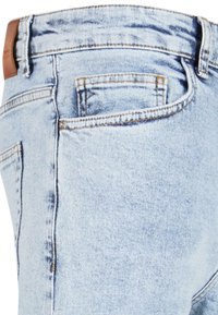 Jeans en denim bleu clair avec un design classique à cinq poches, une texture décolorée et des coutures contrastées, accompagnés d'une étiquette en cuir à la taille.