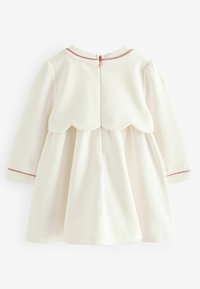 Krémové šaty s dlouhými rukávy, krajkovým zdobením na zádech a zipovým zapínáním. Rukávy jsou jemně lemovány růžovým lemem. Měkká textura látky.