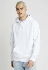 Sweat à capuche blanc avec des rayures verticales bleu clair, poche kangourou, capuche avec cordon de serrage et poignets côtelés. Associé à un jean en denim bleu clair.