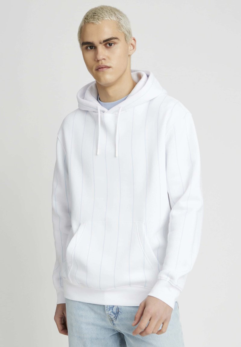 Sweat à capuche blanc avec des rayures verticales bleu clair, poche kangourou, capuche avec cordon de serrage et poignets côtelés. Associé à un jean en denim bleu clair.