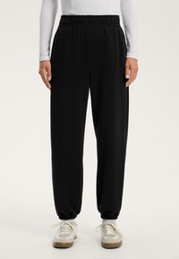 Svarta byxor med elastik i midjan och smalnande mudd, med en mjuk yta. Matchas med ljusa sneakers med beige detaljer.