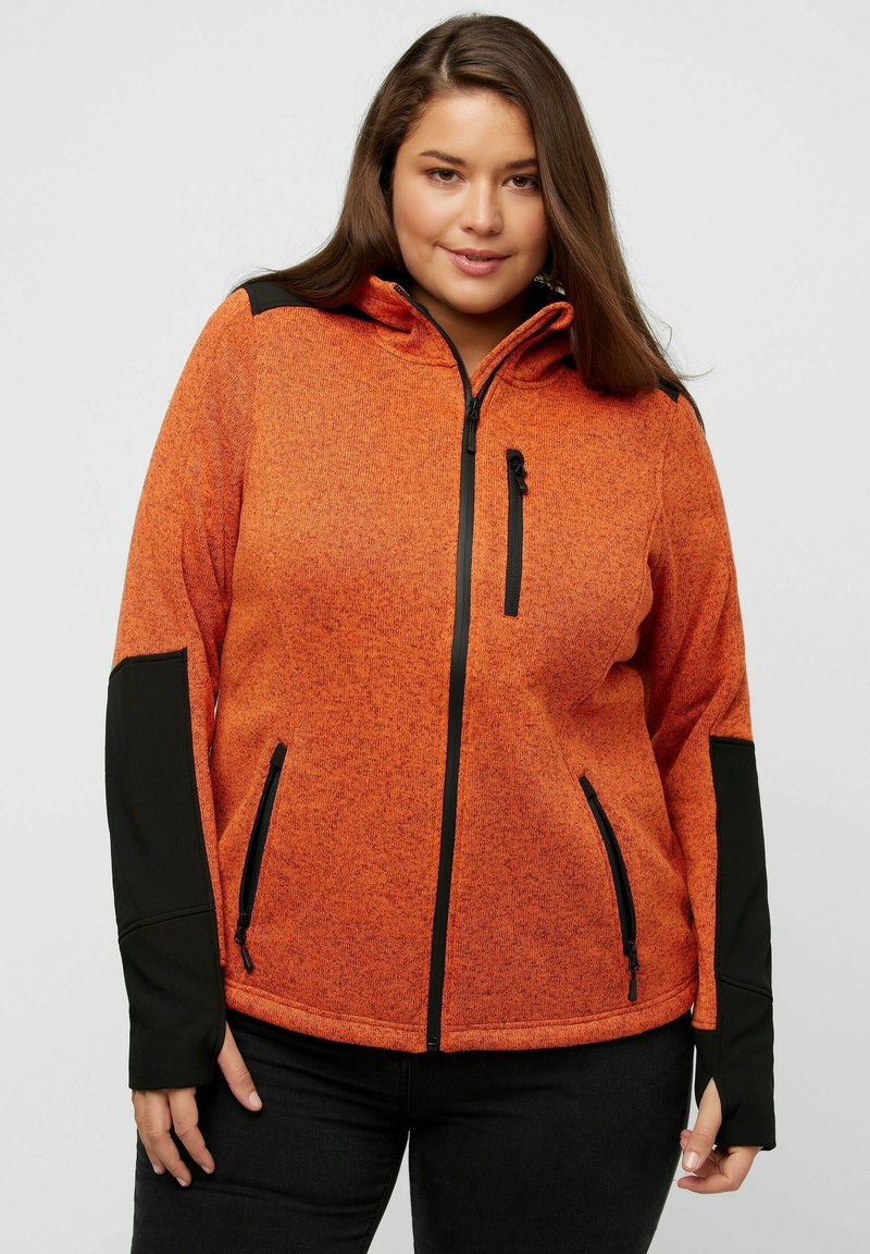 Giacca in pile arancione con accenti neri, zip completa, cappuccio e tasche con zip. Presenta un tessuto testurizzato e aperture per il pollice nei polsini.