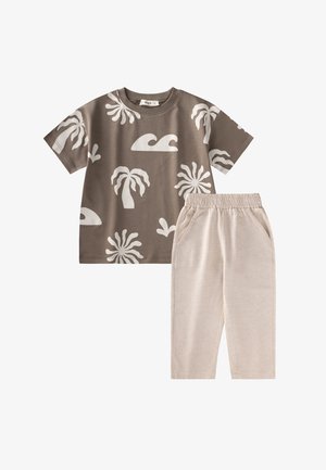 Braunes T-Shirt mit kurzen Ärmeln und weißen tropischen und Wellen-Prints, kombiniert mit hellbeigen Hosen mit elastischem Bund und Taschen.