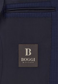 Interior de un traje navy con etiqueta BOGGI MILANO; tejido suave con un discreto detalle de rayas y un diseño de bolsillo elegante.