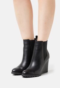 Black leather ankle boots with a wedge heel, elastic side panels, rounded toe, and textured sole. Smooth finish with minimal detailing.