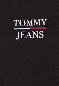 Svart bomullstyg med texten "TOMMY" i stora vita bokstäver och "JEANS" i mindre vita bokstäver, med en tunn röd och vit horisontell linje.