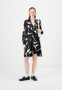 Black wrap dress with white abstract pattern, long sleeves with cuffs, cinched waist, paired with black shoes and light socks.