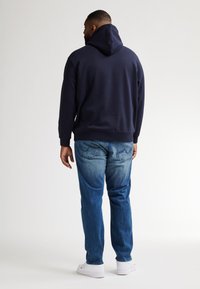 Felpa blu navy con cappuccio regolabile, abbinata a jeans azzurri. La felpa ha polsini e fondo a costine, mentre i jeans presentano un taglio classico.
