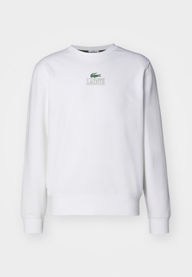 Felpa bianca con maniche lunghe, polsini a coste e scollo rotondo. Presenta il logo verde di Lacoste e testo sul petto. Texture liscia.