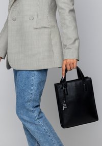 Black leather tote bag with textured finish, square shape, and short handles. Features a silver accent tag with the letter "P."
