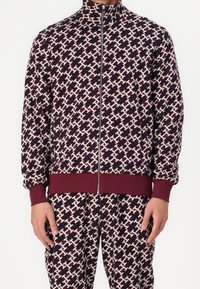 Chaqueta de poliéster con cremallera, con un patrón geométrico en azul marino, blanco y burdeos. Presenta puños y dobladillo acanalados, y bolsillos laterales.