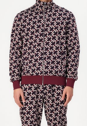 Giacca in poliestere con zip, caratterizzata da un motivo geometrico blu navy, bianco e bordeaux. Presenta polsini e orlo a costine, oltre a tasche laterali.