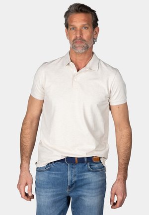 Beige polo-shirt met een klassieke kraag, korte mouwen en drie knopen; gedragen met blauwe spijkerbroek en een blauwe gevlochten riem met bruine accenten.