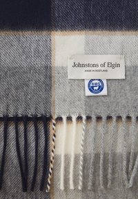 Grå og marineblå uldscarf med et ternet mønster, frynsekant langs kanten og labels med teksten "Johnstons of Elgin" og RWS-certificering.