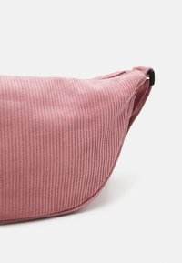 Růžová kordurová kabelka přes rameno s hladkým, zaobleným tvarem a jemnou žebrovanou texturou. Má černý klip jako kovový detail.