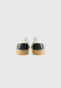 Black and cream leather shoes with a textured back, flat rubber sole, and visible stitching details. Showcasing a classic design.
