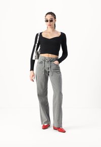 Top corto negro de canalé con mangas largas, pantalones de mezclilla gris de tiro alto y pierna ancha, y zapatos planos rojos de punta. Los accesorios incluyen gafas de sol pequeñas.