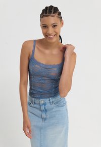 Blauwe kanten camisole met golvende randen, gecombineerd met een lichte denim rok. De top heeft een doorschijnend ontwerp en verstelbare bandjes.
