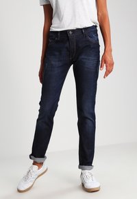 Mörkblå jeans i denim, med smal passform, lätt blekning och uppvikta benslut. Matcher med vita sneakers och en grå t-shirt.