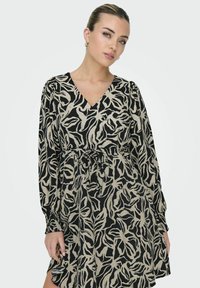 Robe à fleurs noir et beige avec de longues manches bouffantes, décolleté en V et taille élastique. Tissu lisse avec une coupe décontractée.